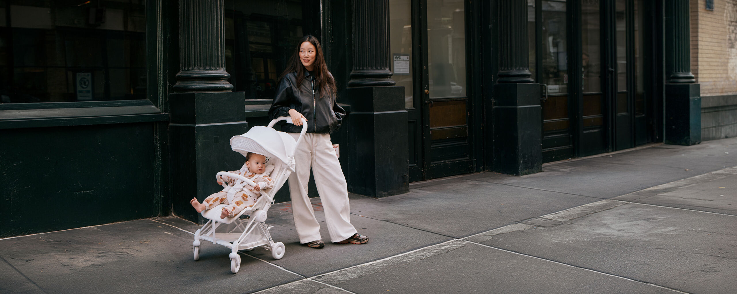 A woman casually leaning against her Urban Mobility Coya, her child sitting inside.