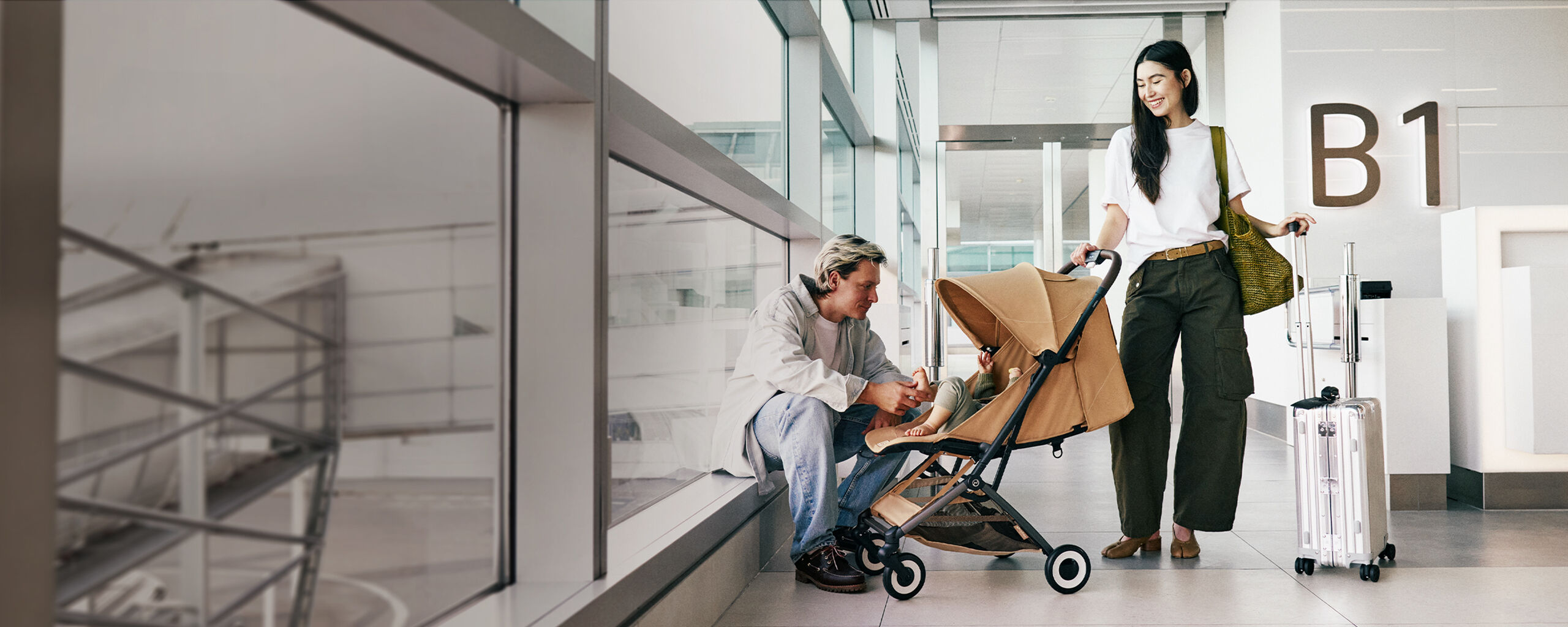Couple at airport gate with child in compact Orfeo stroller and rolling suitcase