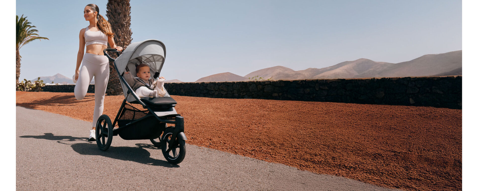 A woman stretching. She's holding onto the handle of her Avi  Spin sport stroller, her child sitting inside.