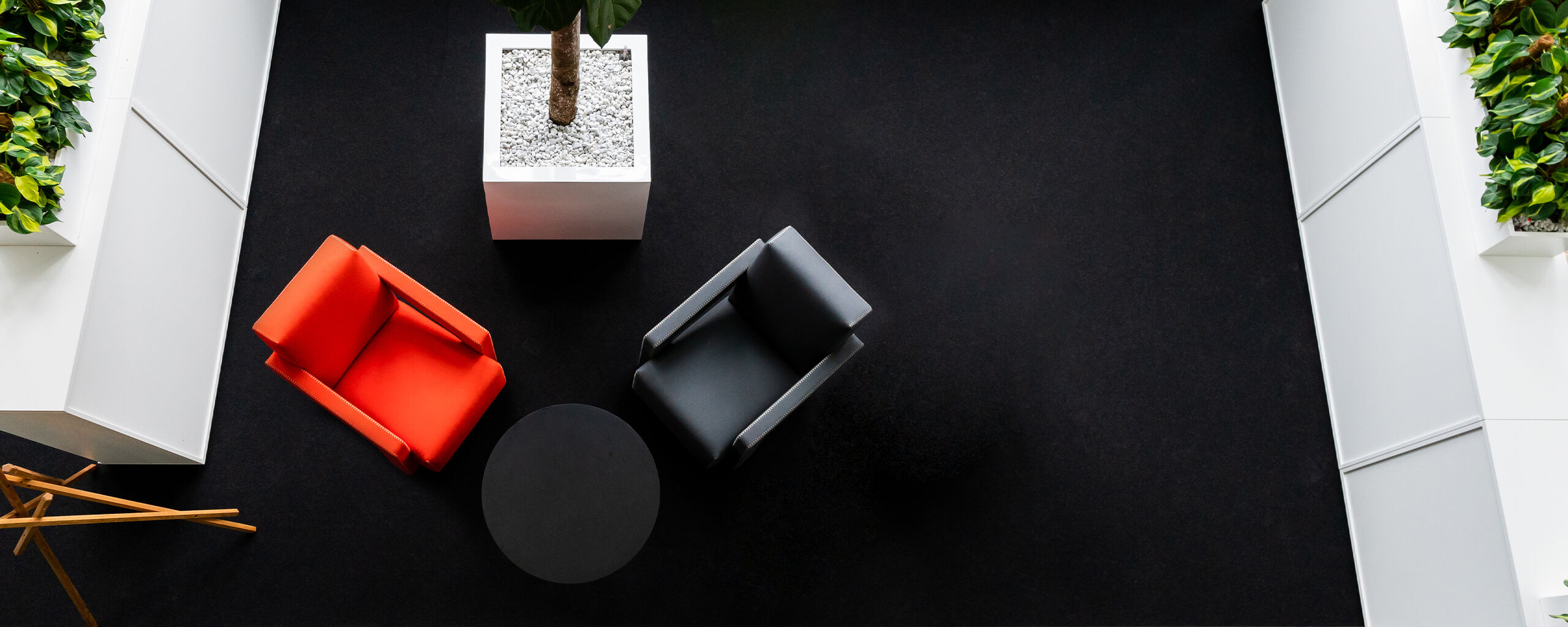 Een moderne wachtruimte met een rode en een grijze fauteuil, een ronde tafel en een grote plantenbak.
