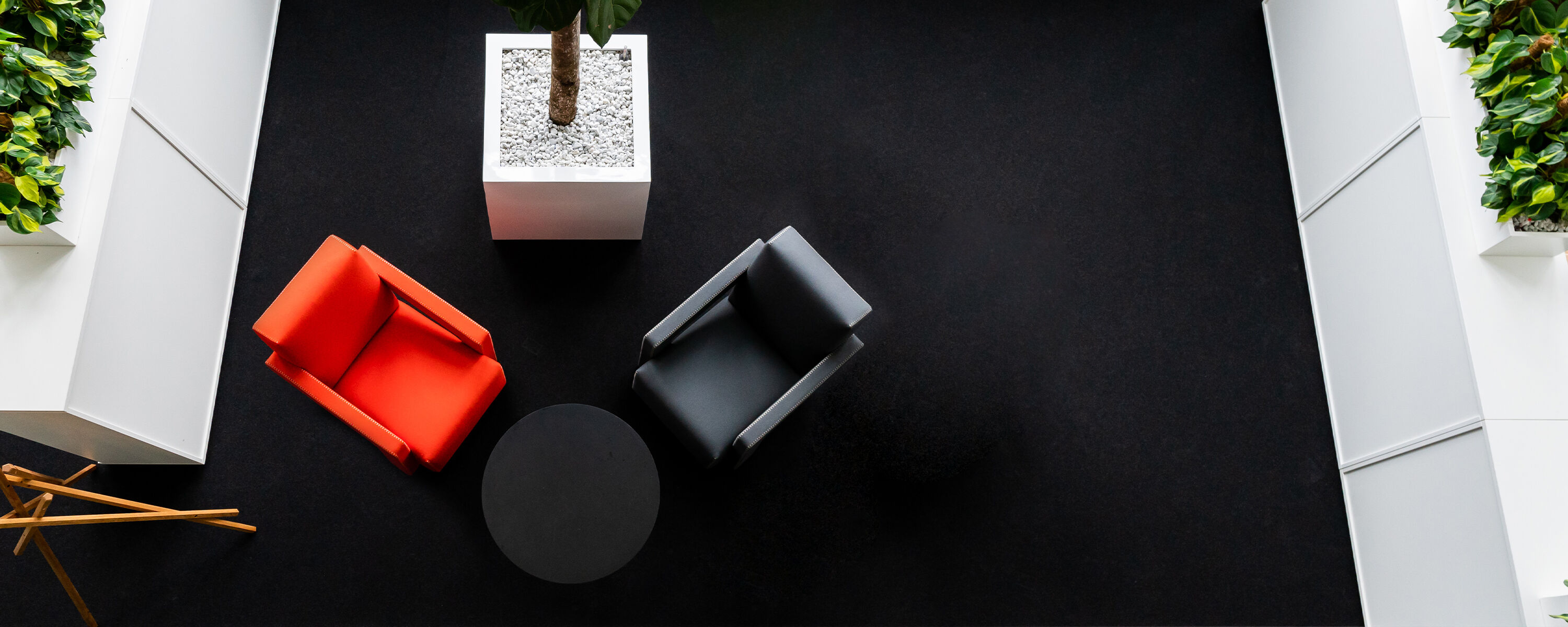 Een moderne wachtruimte met een rode en een grijze fauteuil, een ronde tafel en een grote plantenbak.