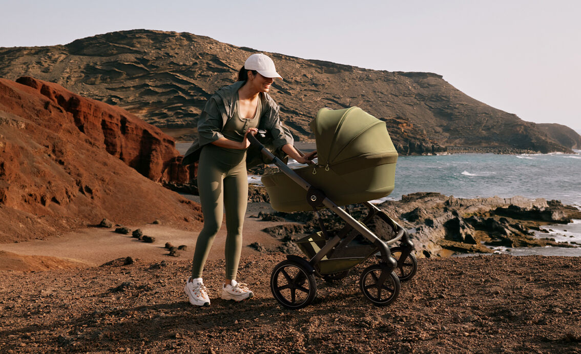 A mother in a sporty outfit checking on her baby in a Talos S Lux stroller next to the ocean.