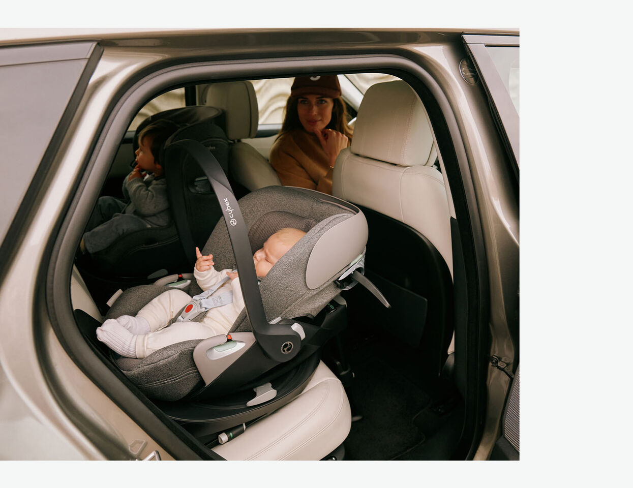 Brünette Frau auf dem Fahrersitz dreht sich um und schaut zu ihrem Baby in einer rückwärtsgerichteten Babyschale, während daneben ein Kleinkind ebenfalls rückwärtsgerichtet in einem CYBEX Kindersitz sitzt.