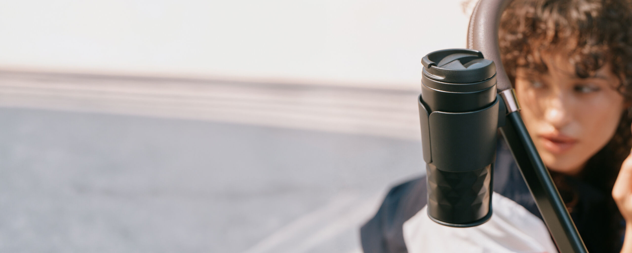 A CYBEX cup holder with a cup inside in focus, a woman on the left blurred.