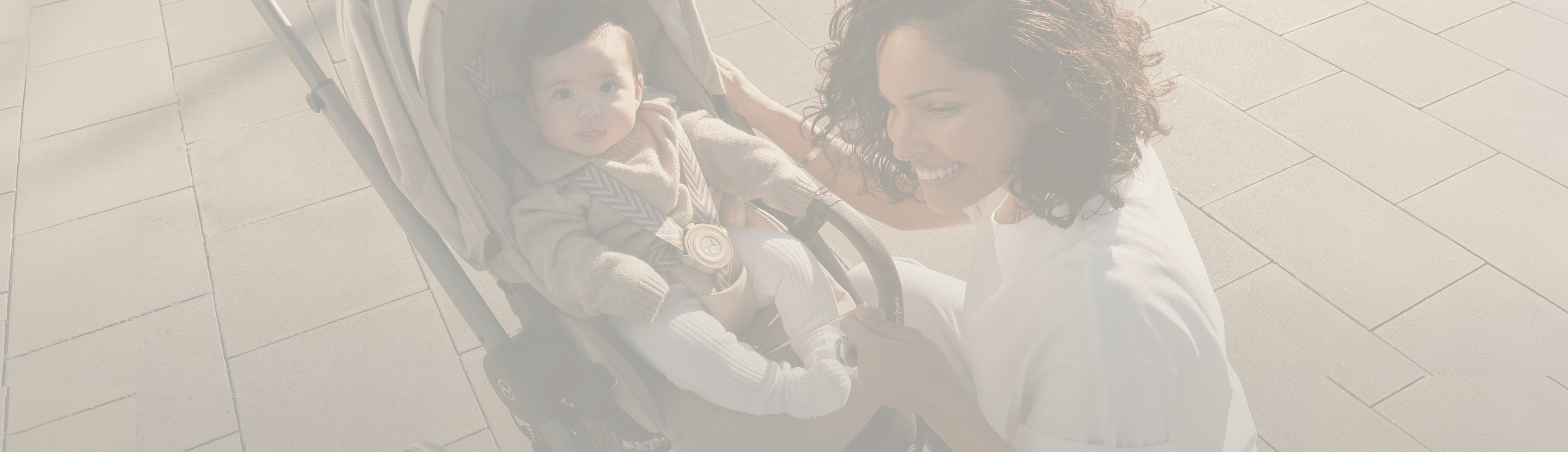 A woman kneeling in front of her CYBEX buggy, her child sitting in it and looking up into the camera.