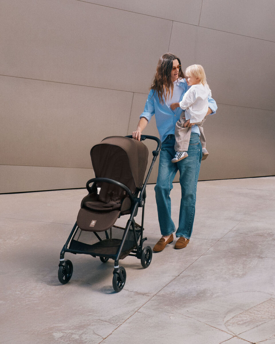 A mother pushes her Melio Carbon stroller, holding her child in her arms.