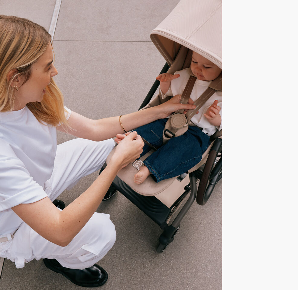 A baby is sitting in the Eezy S Twist +2 360 stroller while the mother fastens the one pull harness.
