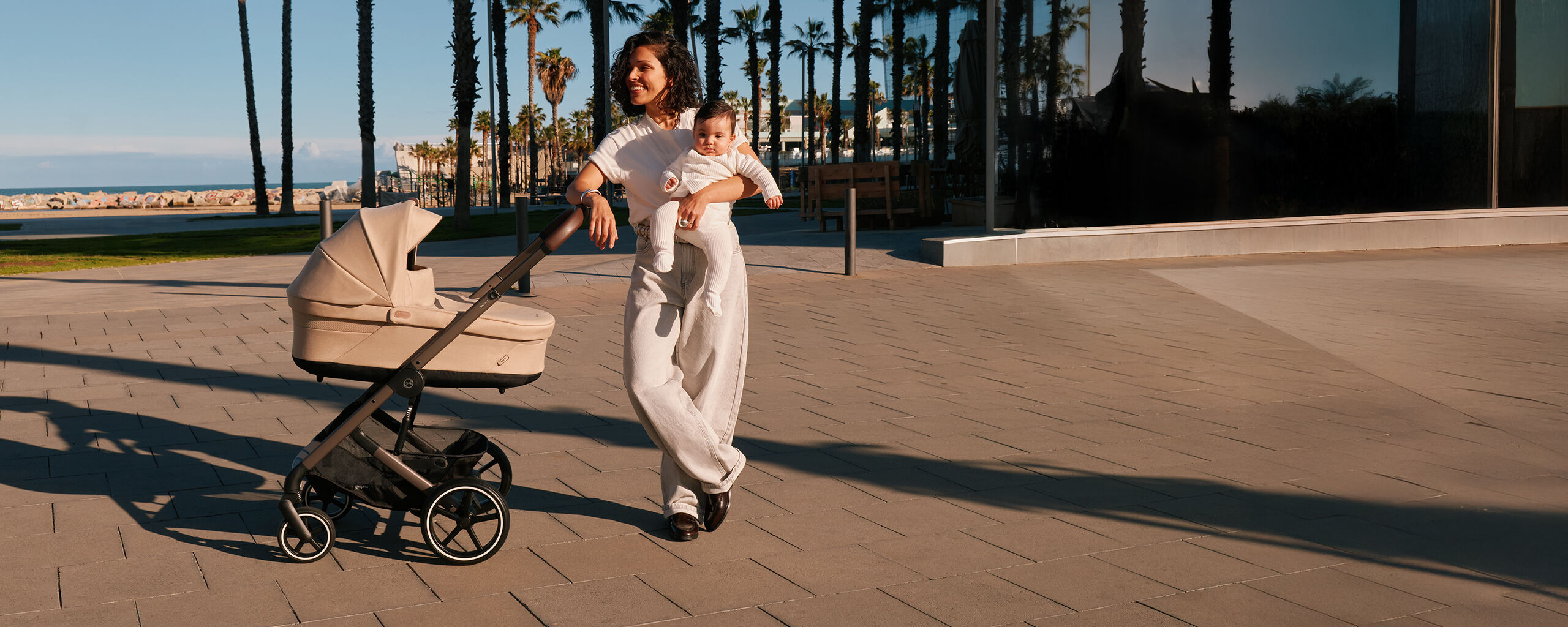 A woman leaning with one arm on the handlebar of her Balios S Lux stroller while holding her baby in the other arm.