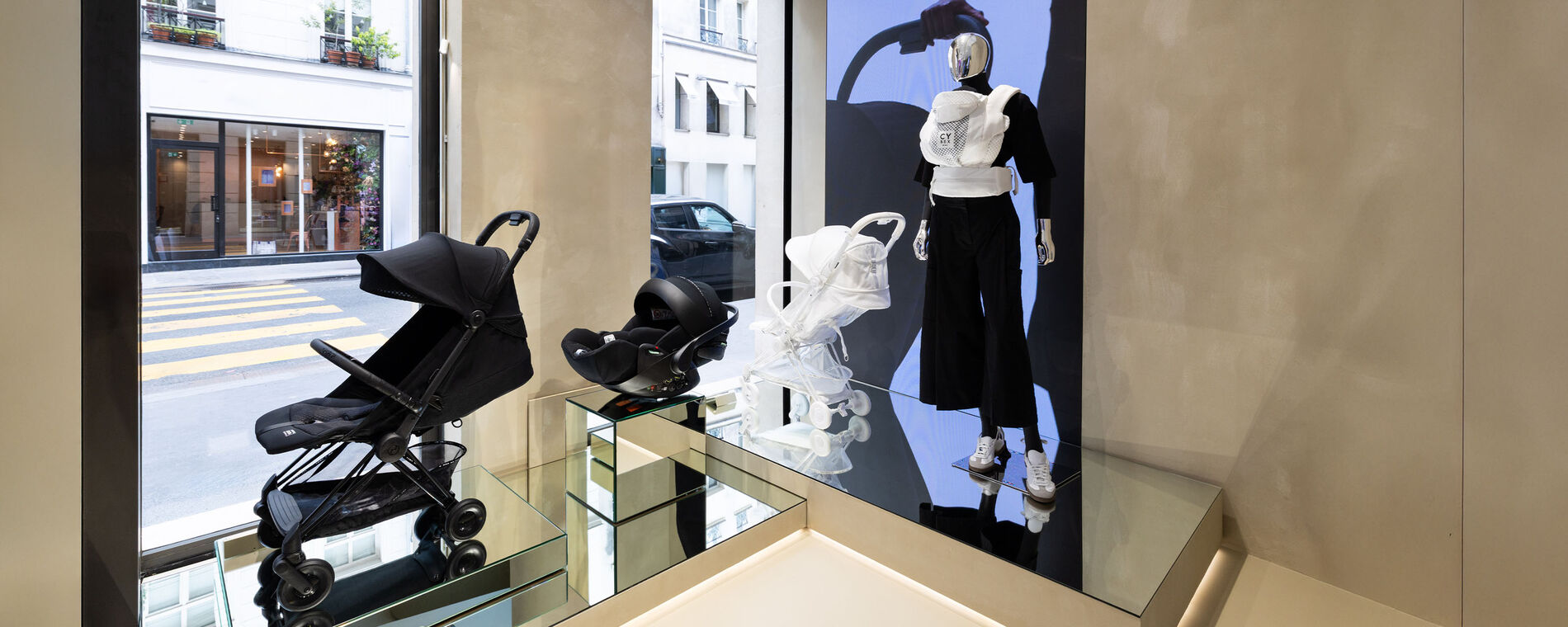 View from inside the CYBEX store towards the street and a visible zebra crossing. The shop window features the CYBEX Coya travel pushchair and pushchairs from the Urban Mobility collection.