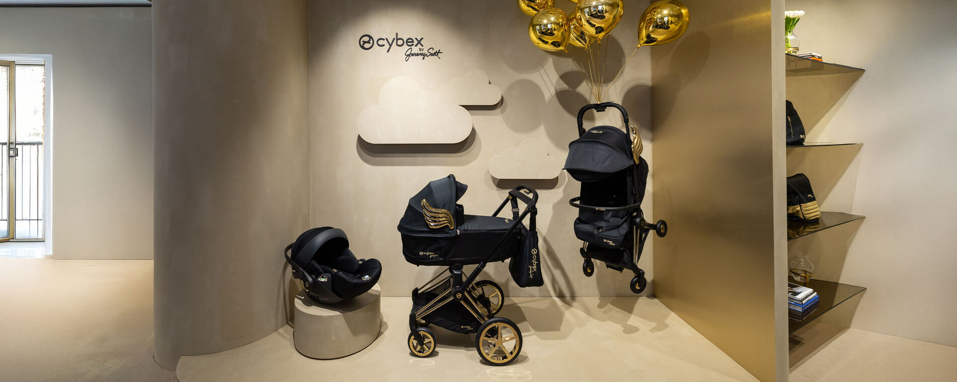 CYBEX by Jeremy Scott ‘Wings’ collection with golden balloons, stylishly displayed against a beige wall.