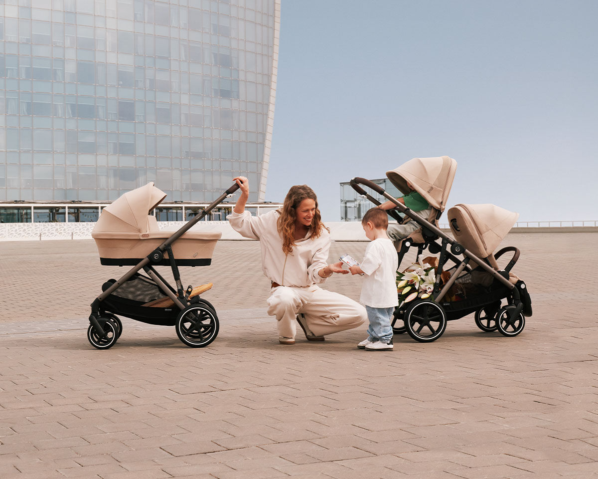 Man pushing a pram with a baby car seat against a yellow background.