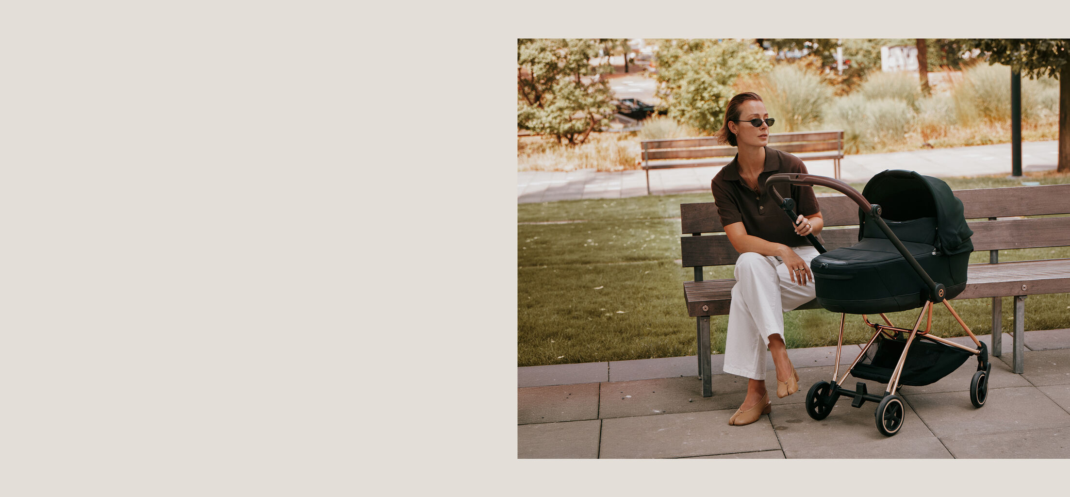 A mother sitting on a bench, one hand on the handle of her CYBEX pushchair..