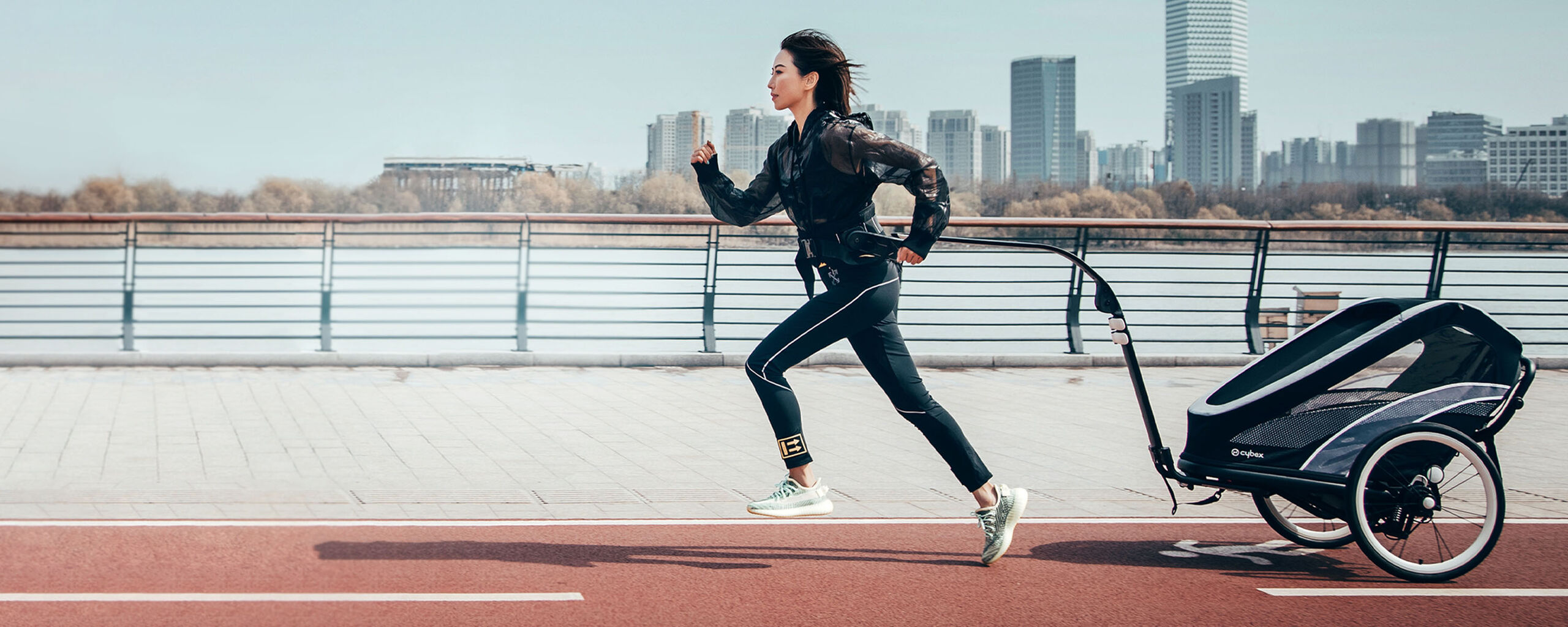A woman jogging on a promenade, pulling a child trailer behind her.
