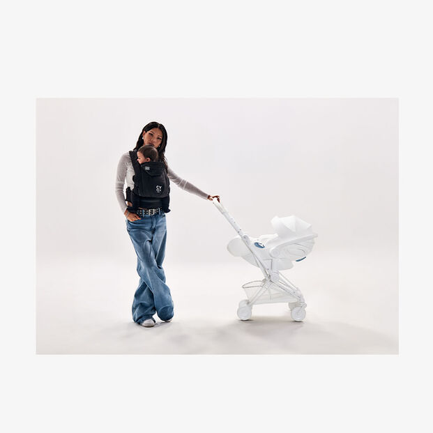 A woman in casual clothing crouches next to a modern white sculpture in a minimalist space.