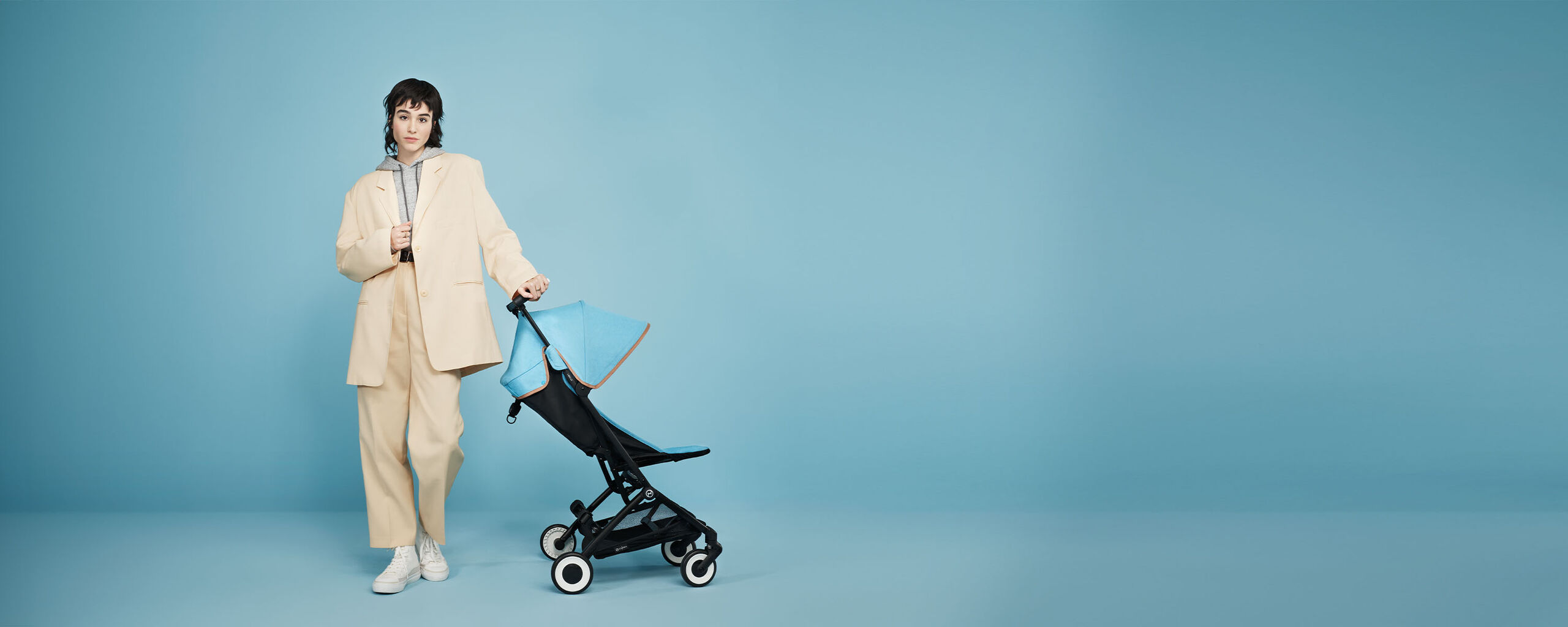 Person standing next to a Libelle smallest fold stroller against a blue background.