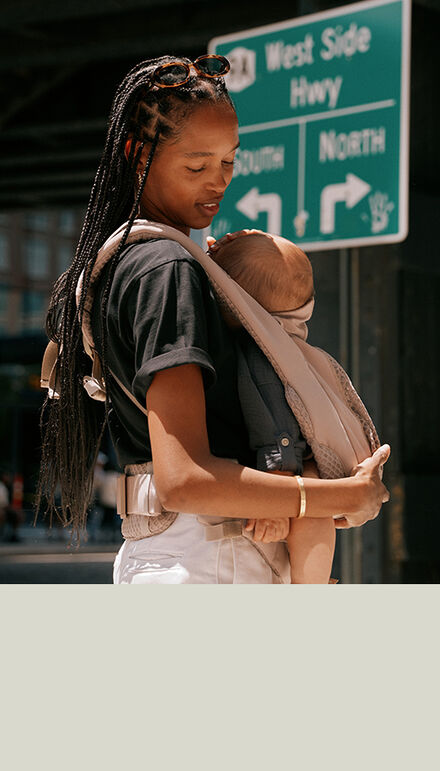 A mother holding her baby in a Coya Carrier, looking down at them. 