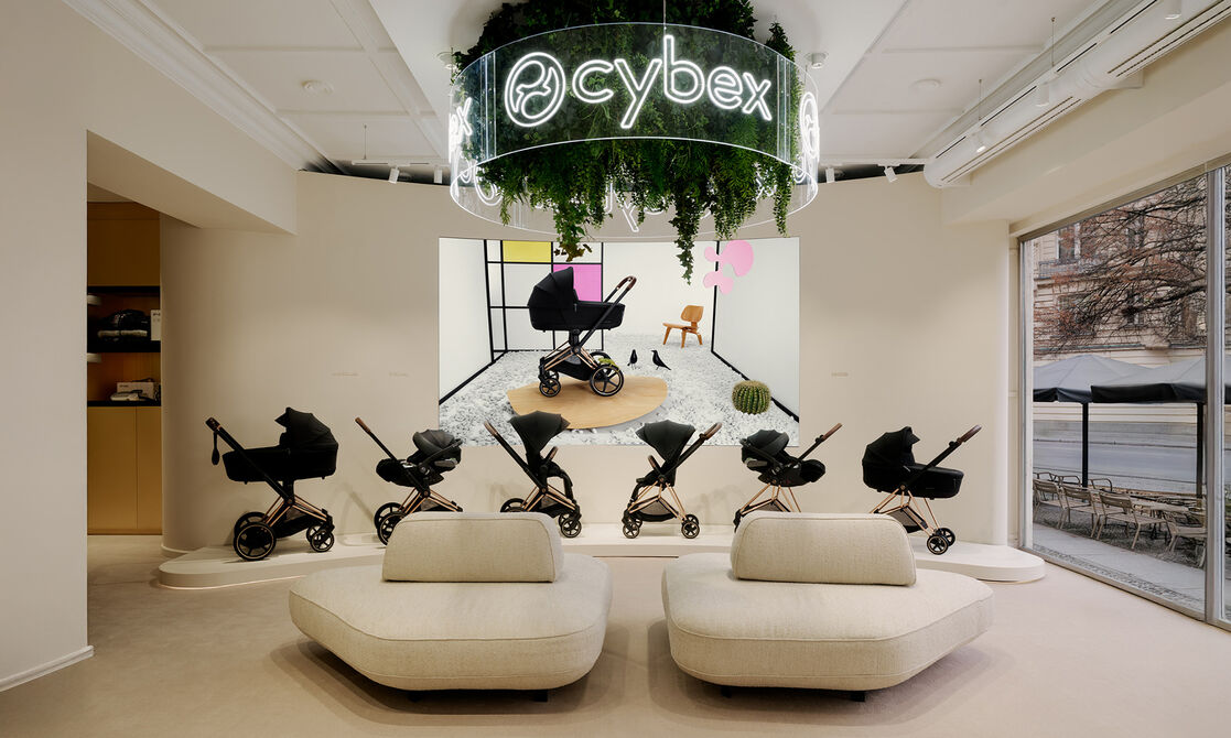 CYBEX logo hanging from the ceiling. Underneath, two couches and a bunch of CYBEX strollers on display.