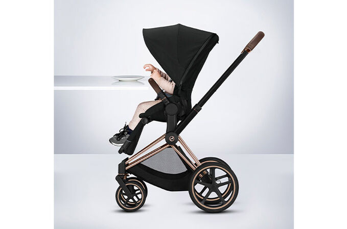 Ein Bild des CYBEX Platinum e-Priam 1  Jeremy Scott - Cherubs Stroller, das das Merkmal Sitz auf Tischhöhe hervorhebt.