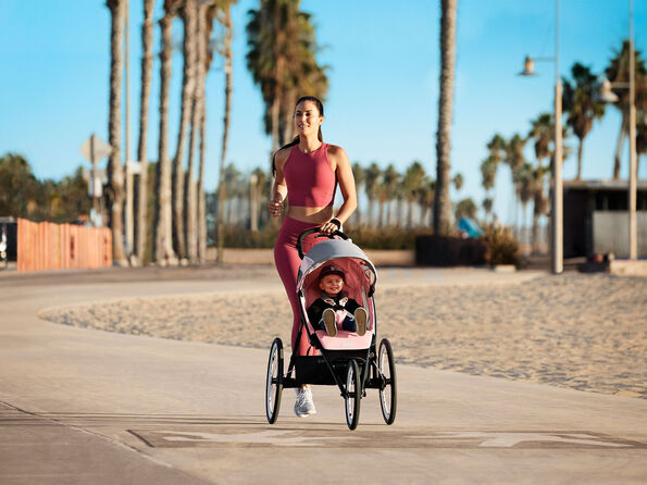 Woman jogging on a promenade with a Zeno jogging stroller, with a child seated inside.