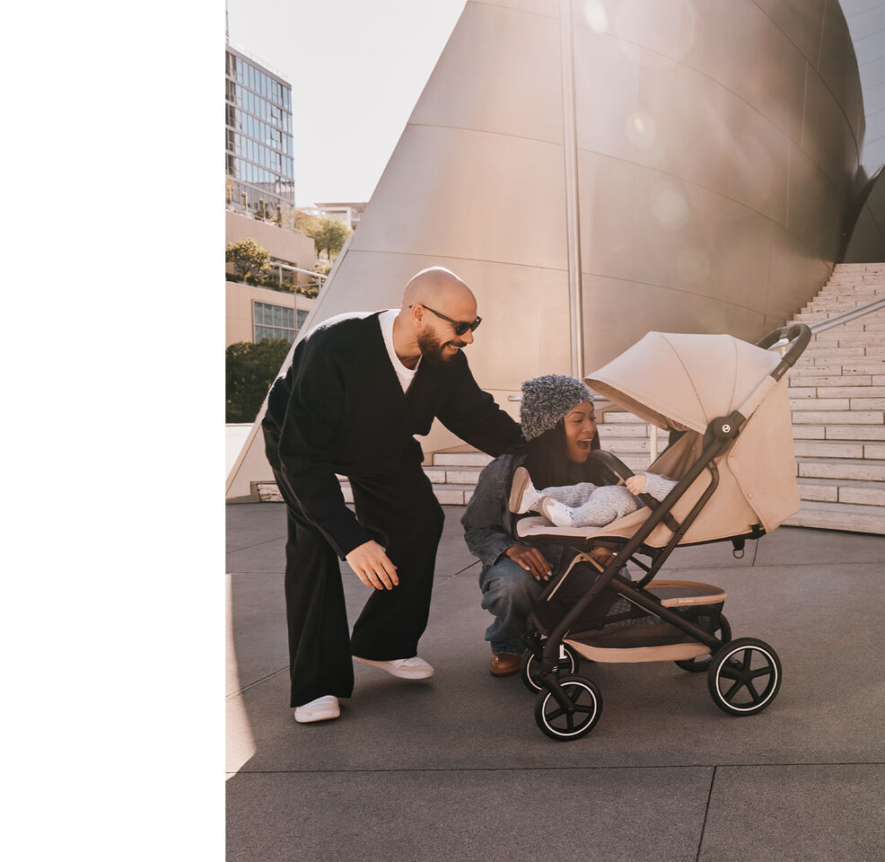 A man and a woman check on their baby in a Beezy buggy, both of them laughing.