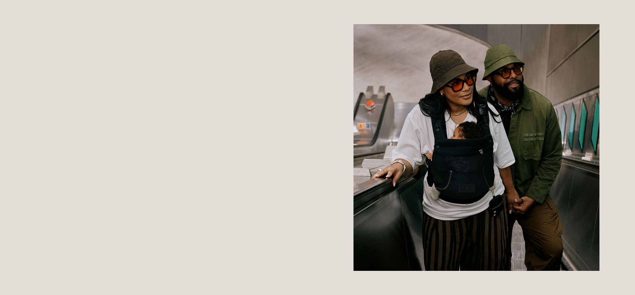 A woman and a man going up an escalator. The woman has her baby in a CYBEX carrier against her chest.