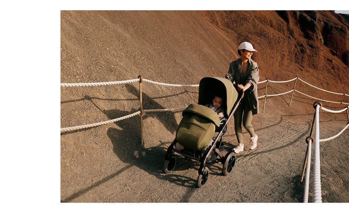A mother pushing her child in a Talos S Lux stroller up a path. It looks like a hiking trail.