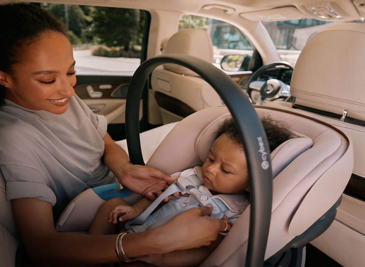 Parent securing their baby in an infant car seat inside a vehicle.