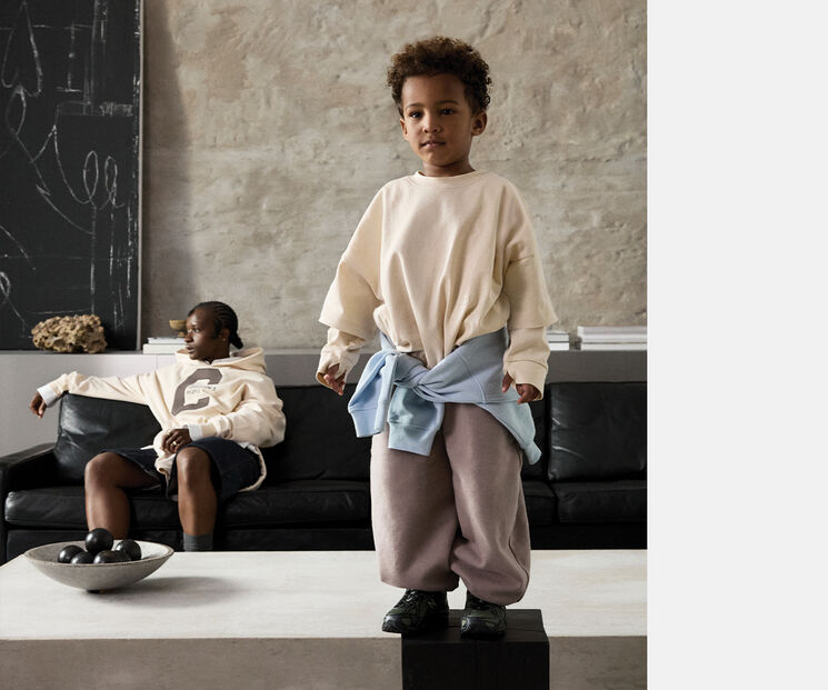 A parent and child in a living room. The parent is sitting on the couch, the child is standing on the table in front of them.