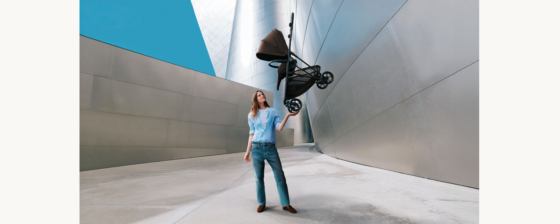 A woman lifts the Melio Carbon lightweight stroller against a bright background.