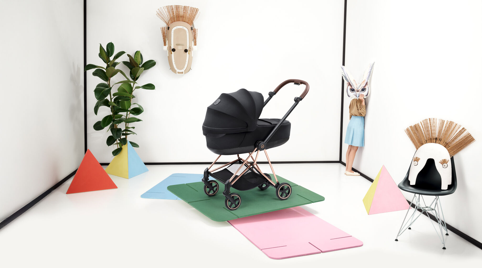 A CYBEX Mios stroller. On the left is a girl facing a wall, her face hidden behind an owl mask.