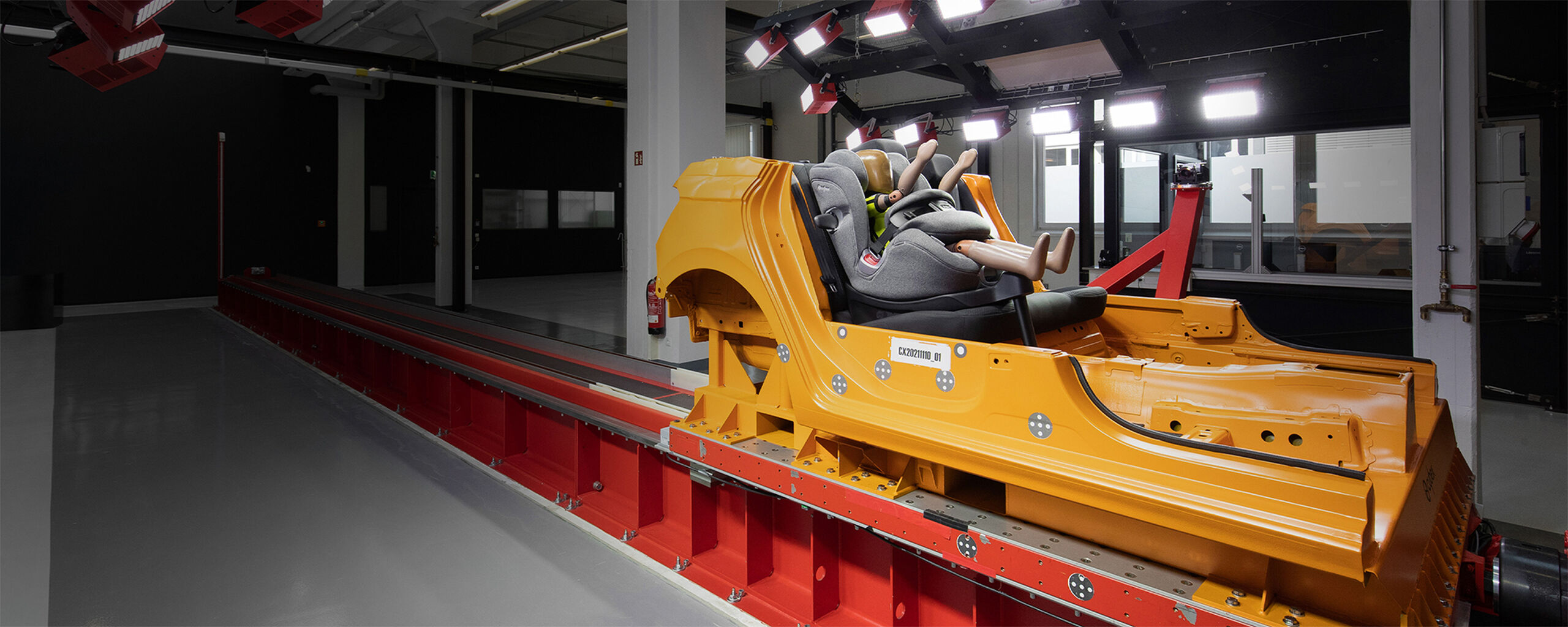 A crash test facility with a crash test vehicle. Inside the vehicle is a CYBEX car seat with a crash test dummy sitting inside.