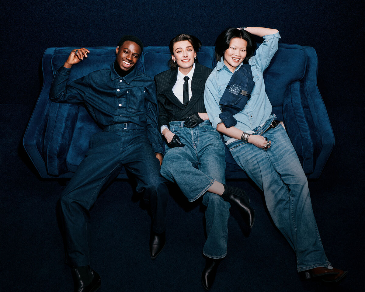 A man and two women sitting on a denim couch, the woman on the right wearing a Rebellious Luxury Belt Bag around her.