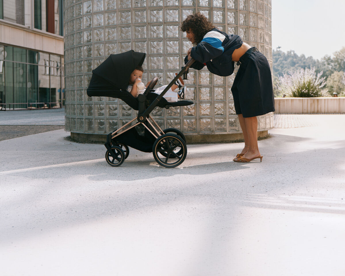 A mother leaning against the handlebar of her stroller, her child inside.