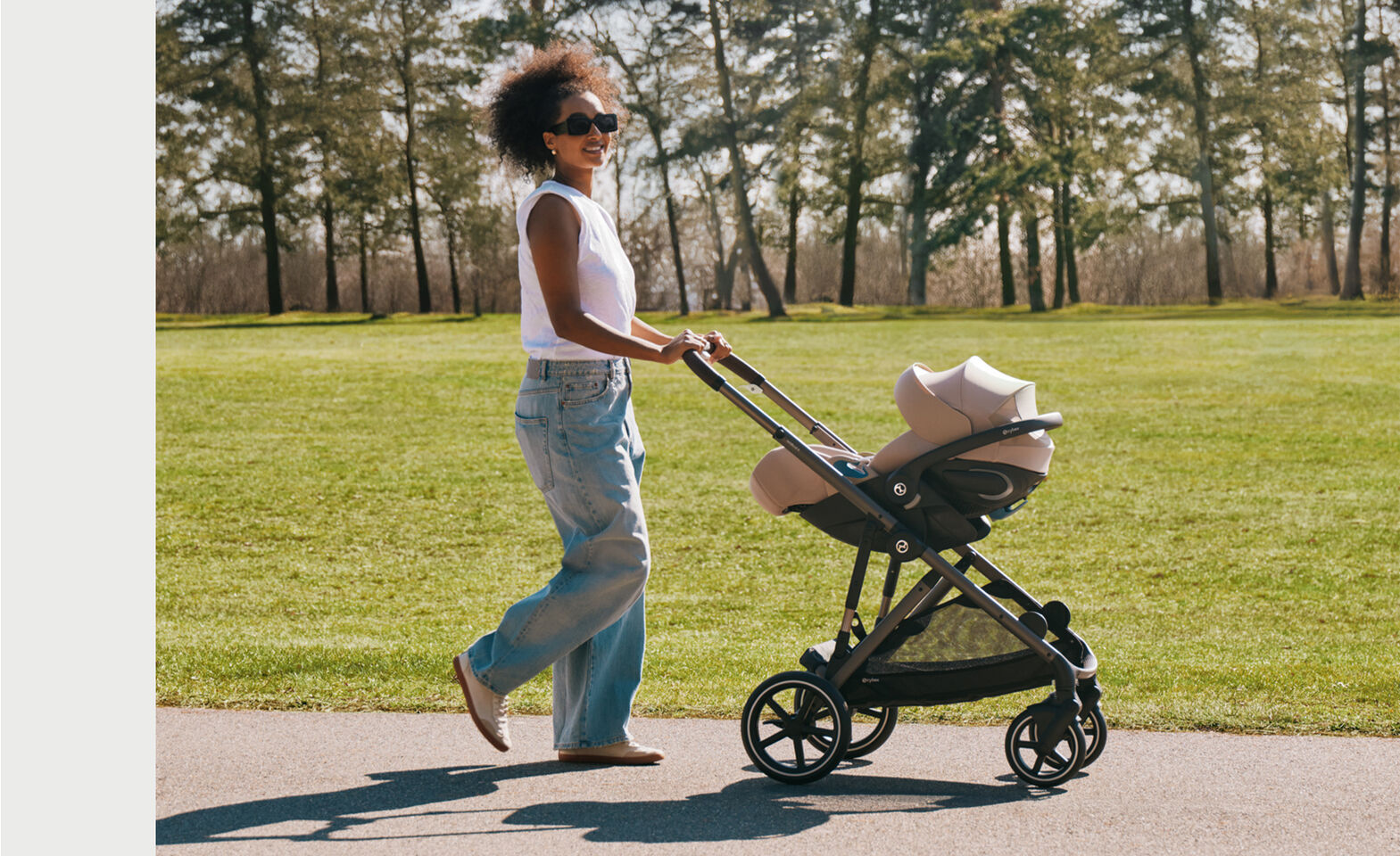 A mother pushing her stroller with a Cloud G Pro infant car seat attached to the frame through a park.