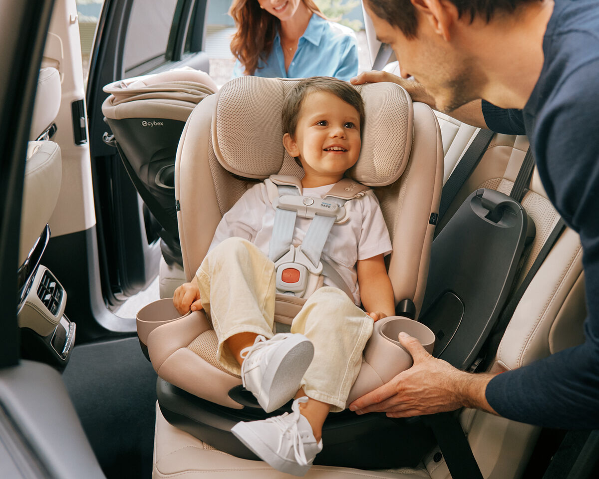 Child happily seated in a car seat while an adult adjusts the seat.