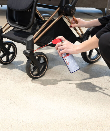 Een vrouw met ringen om haar vingers spuit iets op de wielen van een CYBEX kinderwagen.