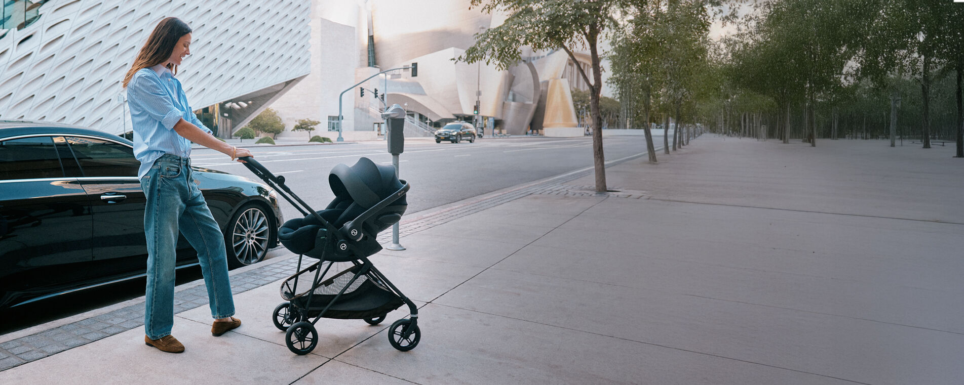 A mother pushing a Melio Carbon with an infant car seat attached.