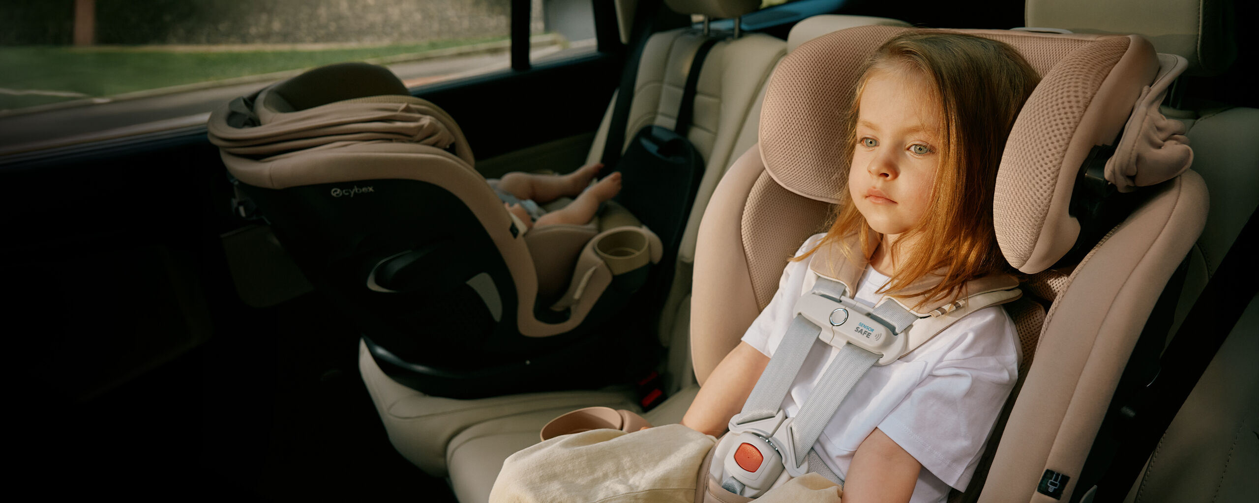 A woman stands next to a black car holding a baby seat with a baby inside.
