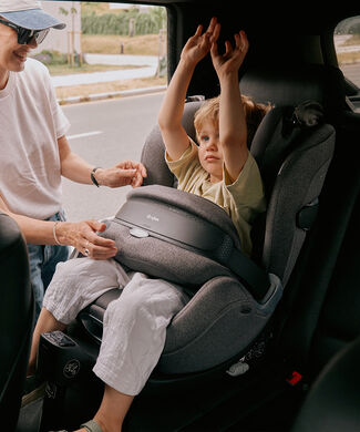 Matka nastavuje štít proti nárazu autosedačky CYBEX. Její syn sedí v autosedačce a ruce má ve vzduchu.