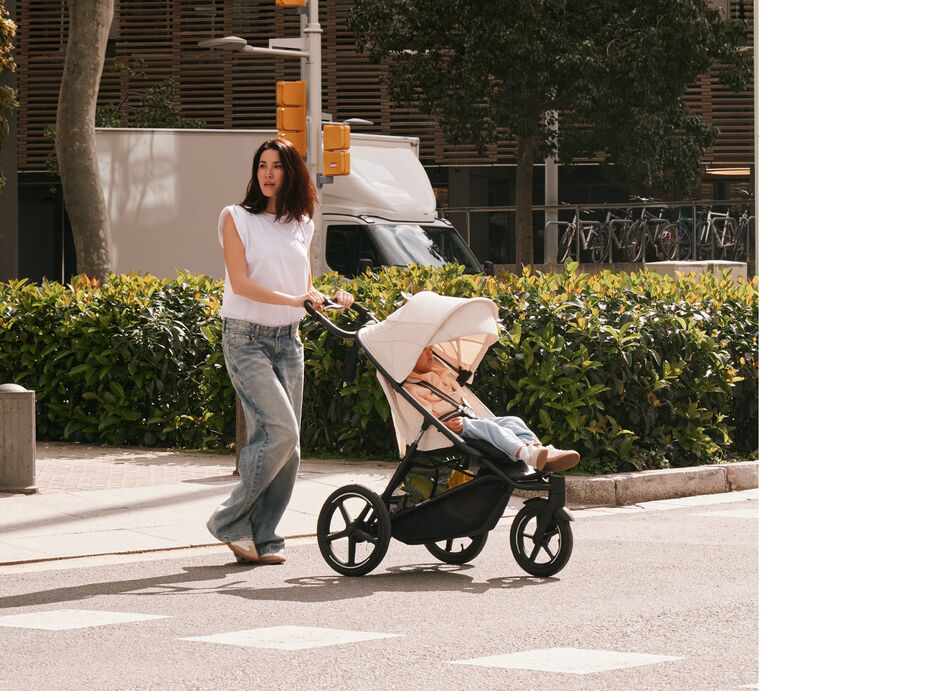 A woman crossing the street with an Avi Spin stroller with a seat pack attached.