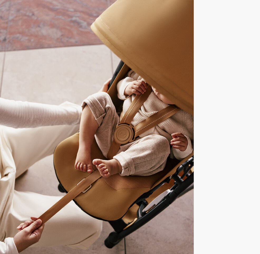 A woman pulling the one-pull harness of the Libelle with her child inside securely tight.