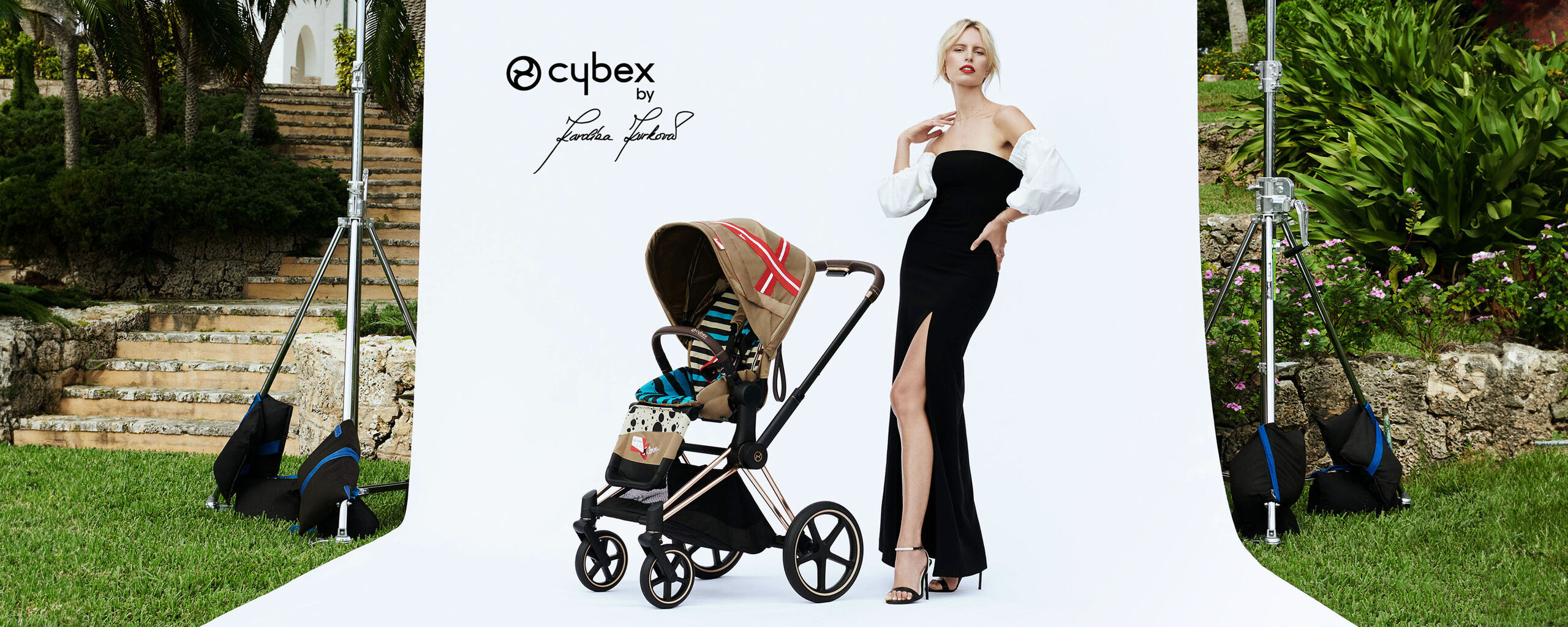 Un elegante passeggino di Cybex by Karolina Kurkova accanto a una persona in abito nero con maniche bianche su uno sfondo bianco.