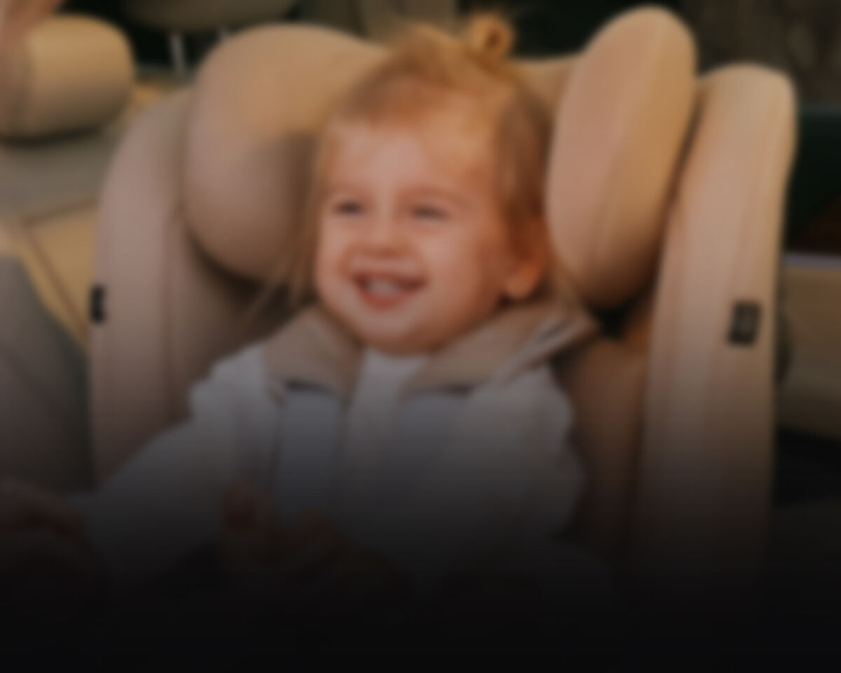 Blurred image of a child laughing, sitting in a CYBEX car seat.