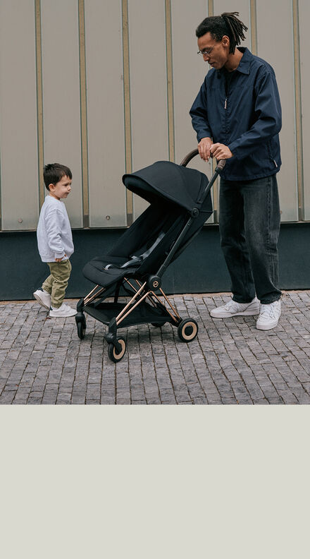 A father holding on to a Coya lightweight stroller with his son next to the stroller.