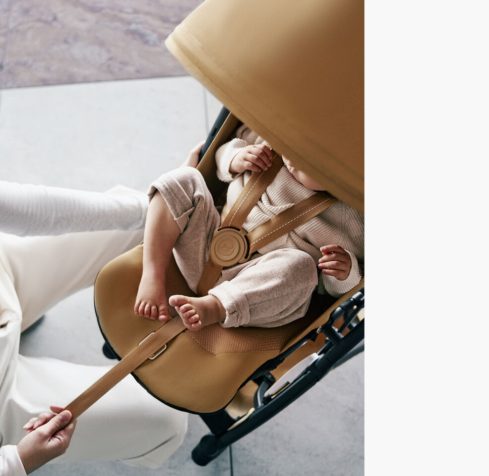 Een vrouw die het one-pull harness van de Libelle strak aantrekt terwijl haar kind er veilig in zit.