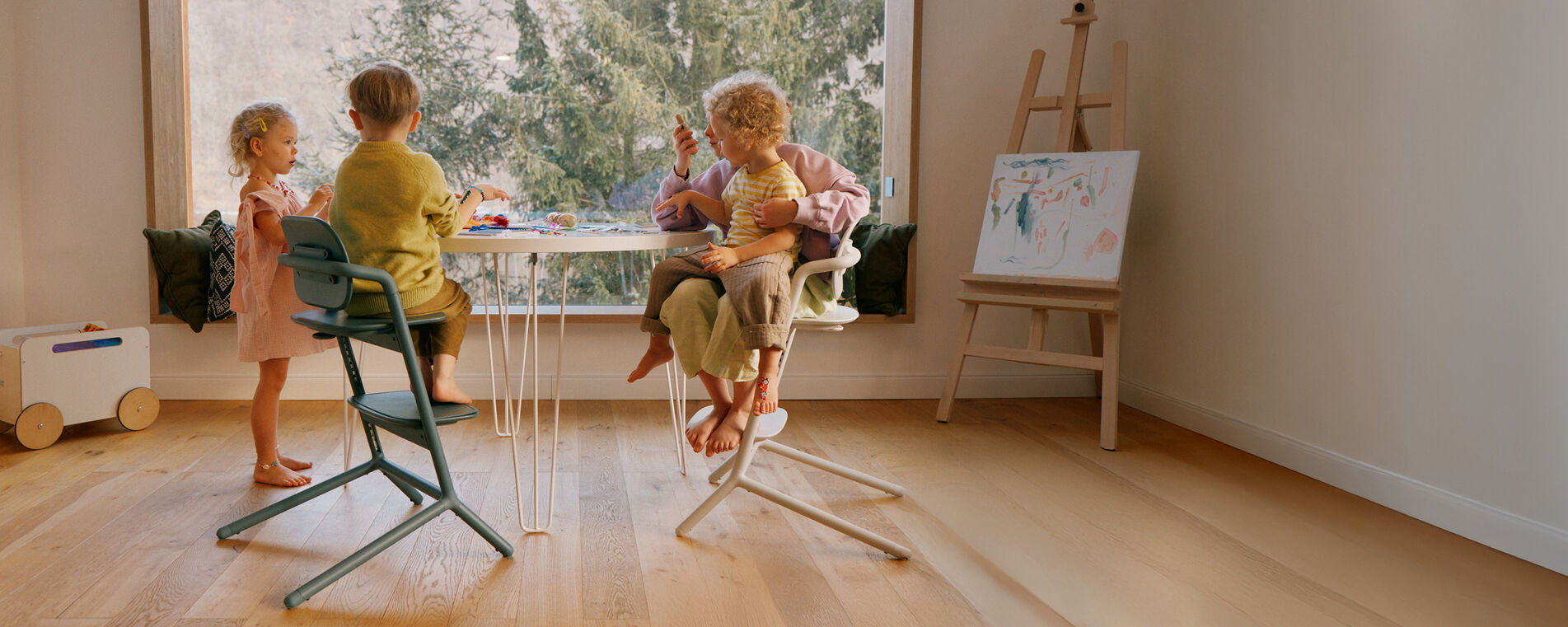 Vier Kinder sitzen an einem Tisch und basteln, zwei Kinder sitzen auf einem Lemo Hochstuhl.