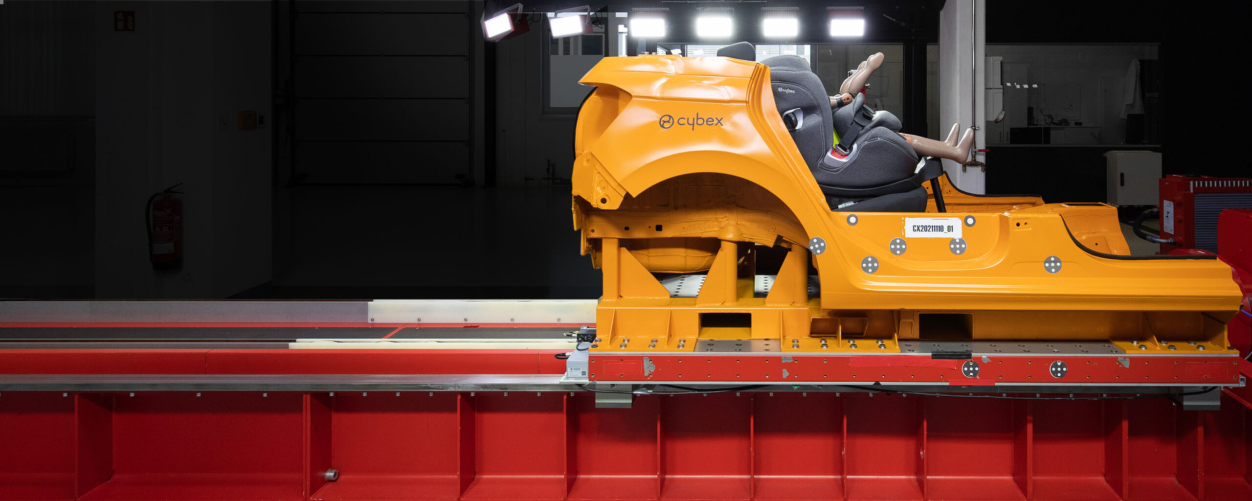 En orange krocktestsl&auml;de med en Cybex bilbarnstol och en docka i en testanl&auml;ggning.