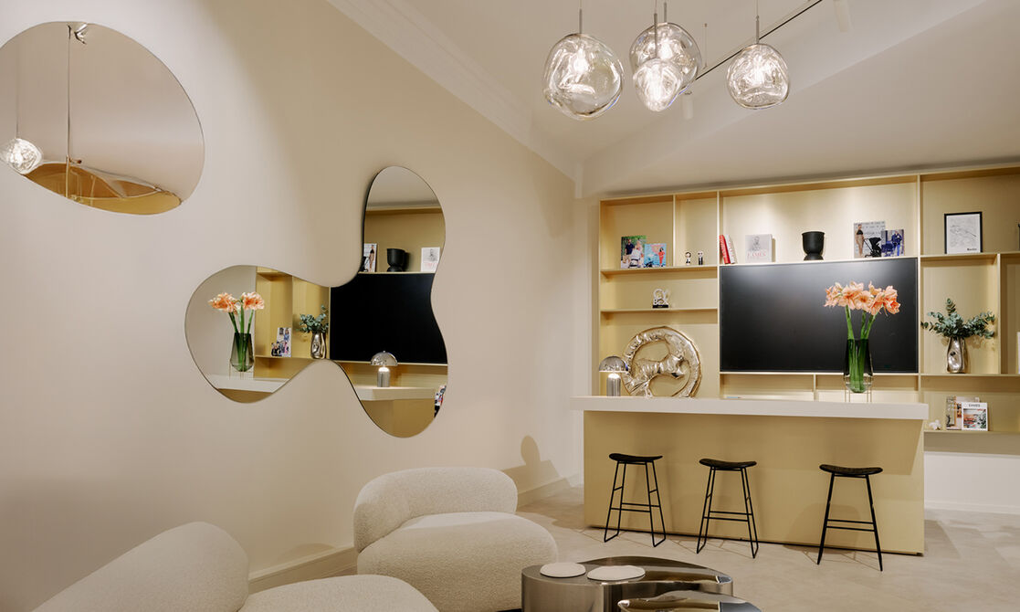 Two mirrors on the left hanging on a wall. There's a display that almost looks like part living room, part kitchen with three barstools. It all looks homey.