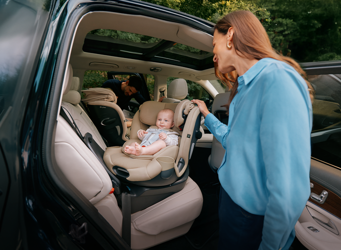 A baby sitting inside a CYBEX car seat, the mother is turning the car seat towards the door.