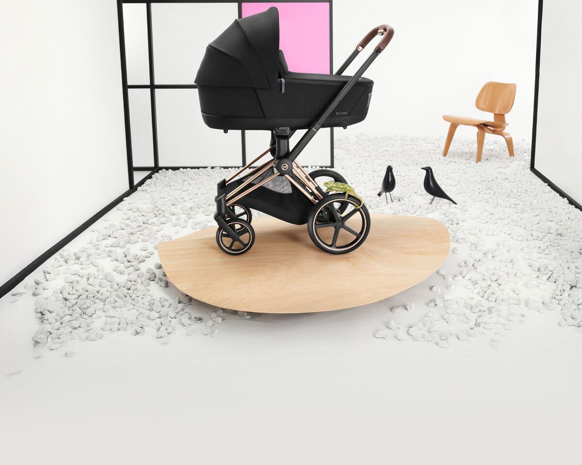 CYBEX Priam in front of white background with wooden accents and a wooden chair behind it, as well as two fake crows.